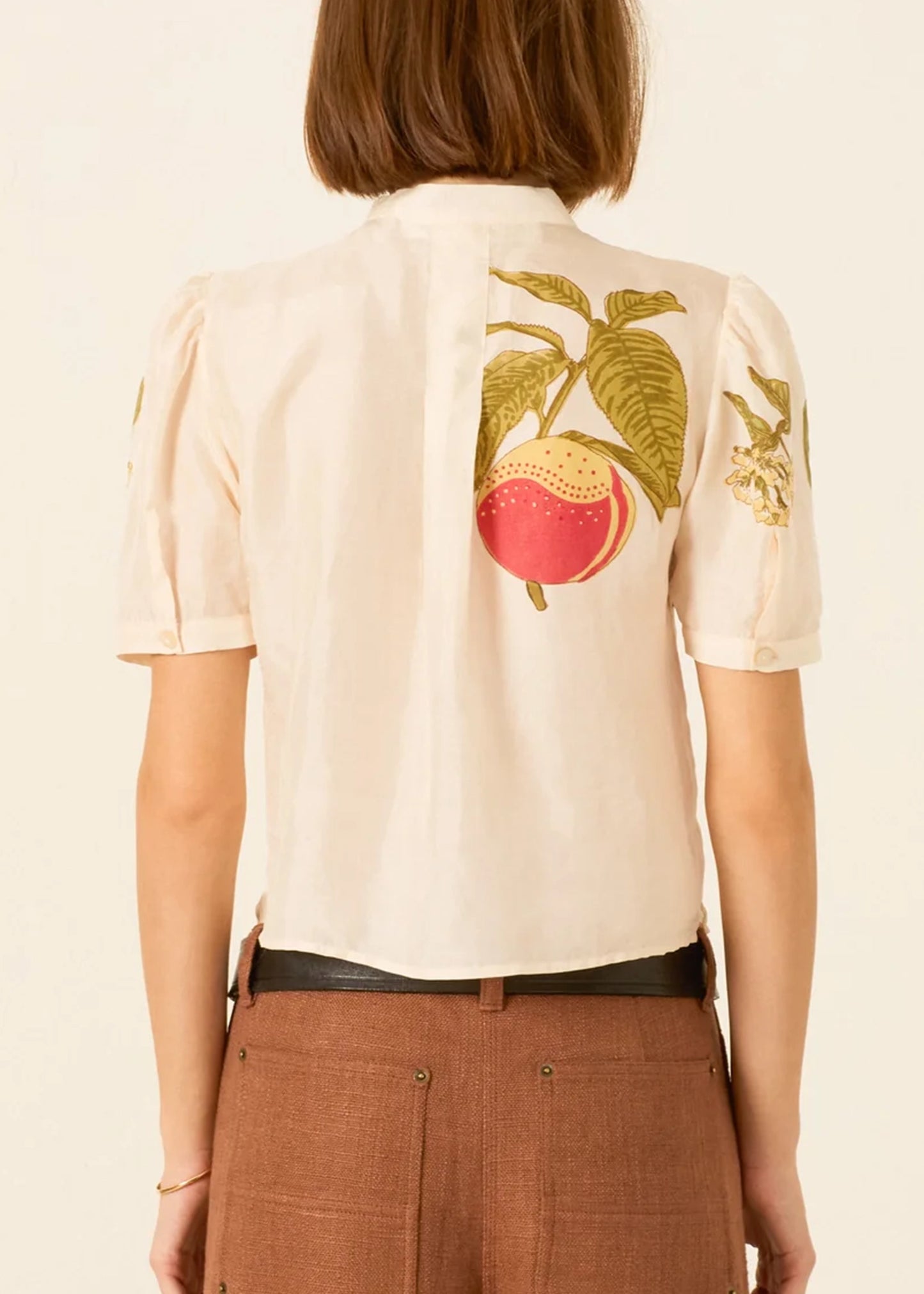 a cream-colored short-sleeve blouse by Alix of Bohemia with a tie-neck detail and colorful embroidered fruit motifs