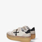 A low-top platform sneaker by Premiata, featuring a cream and beige suede and mesh upper, a black cross logo on the side, gold-tone hardware, and a thick tan gum sole.